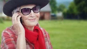 Ältere Frau mit Sonnebrille E.COOLINE kühlendem Halstuch rot telefoniert mir Händy im Grünen