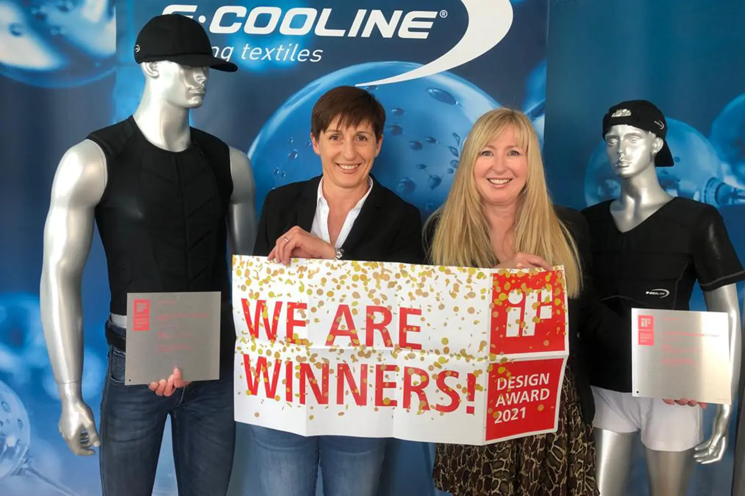 Sabine Stein (links) und Gabriele Renner (rechts) mit IF Award Auszeichnung "We are winners" zwischen Puppen mit E.COOLINE Produkten